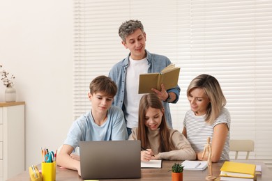 Photo of Parents and their children doing homework with laptop at table indoors