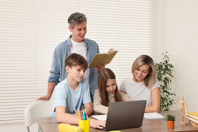 Photo of Parents and their children doing homework with laptop at table indoors