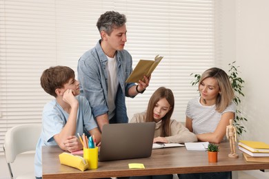 Photo of Parents and their children doing homework with laptop at table indoors