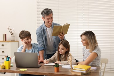 Photo of Parents and their children doing homework with laptop at table indoors