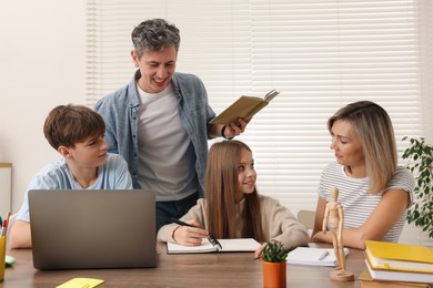 Photo of Parents and their children doing homework with laptop at table indoors