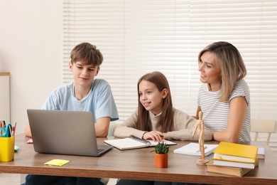 Photo of Smiling mother helping her children with homework at table indoors