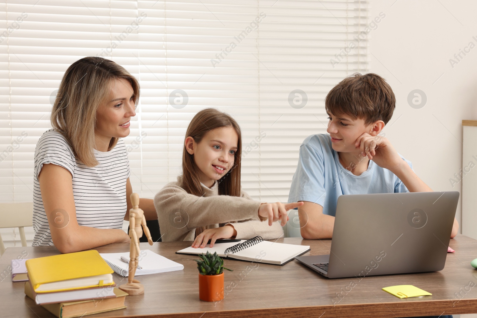 Photo of Smiling mother helping her children with homework at table indoors