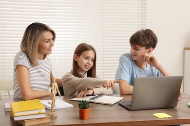 Photo of Smiling mother helping her children with homework at table indoors