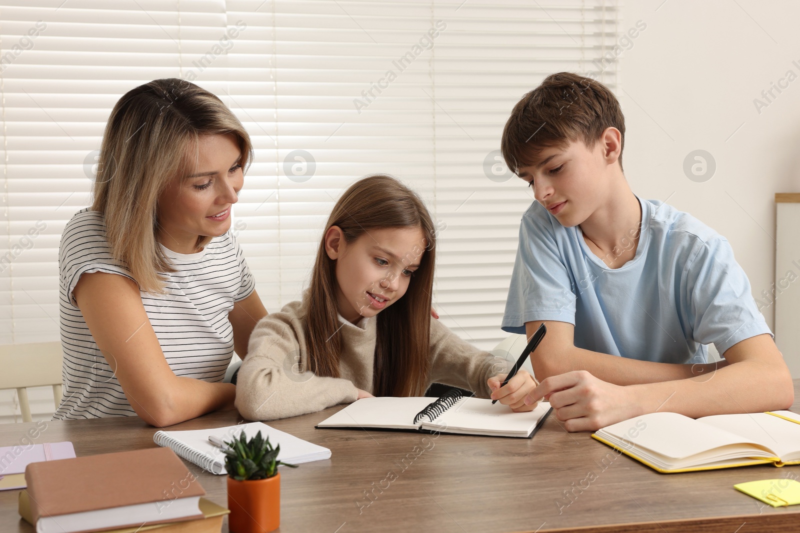 Photo of Smiling mother helping her children with homework at table indoors