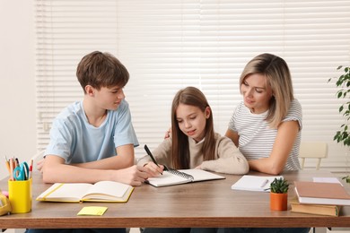 Photo of Smiling mother helping her children with homework at table indoors