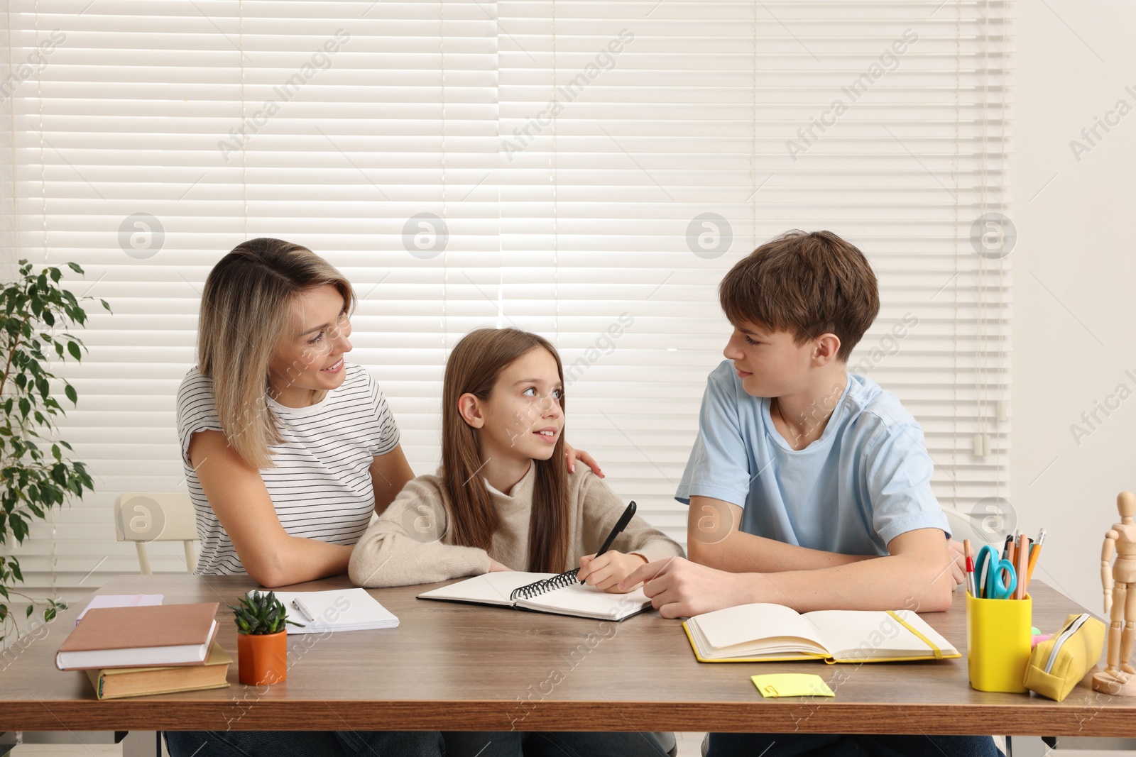 Photo of Smiling mother helping her children with homework at table indoors