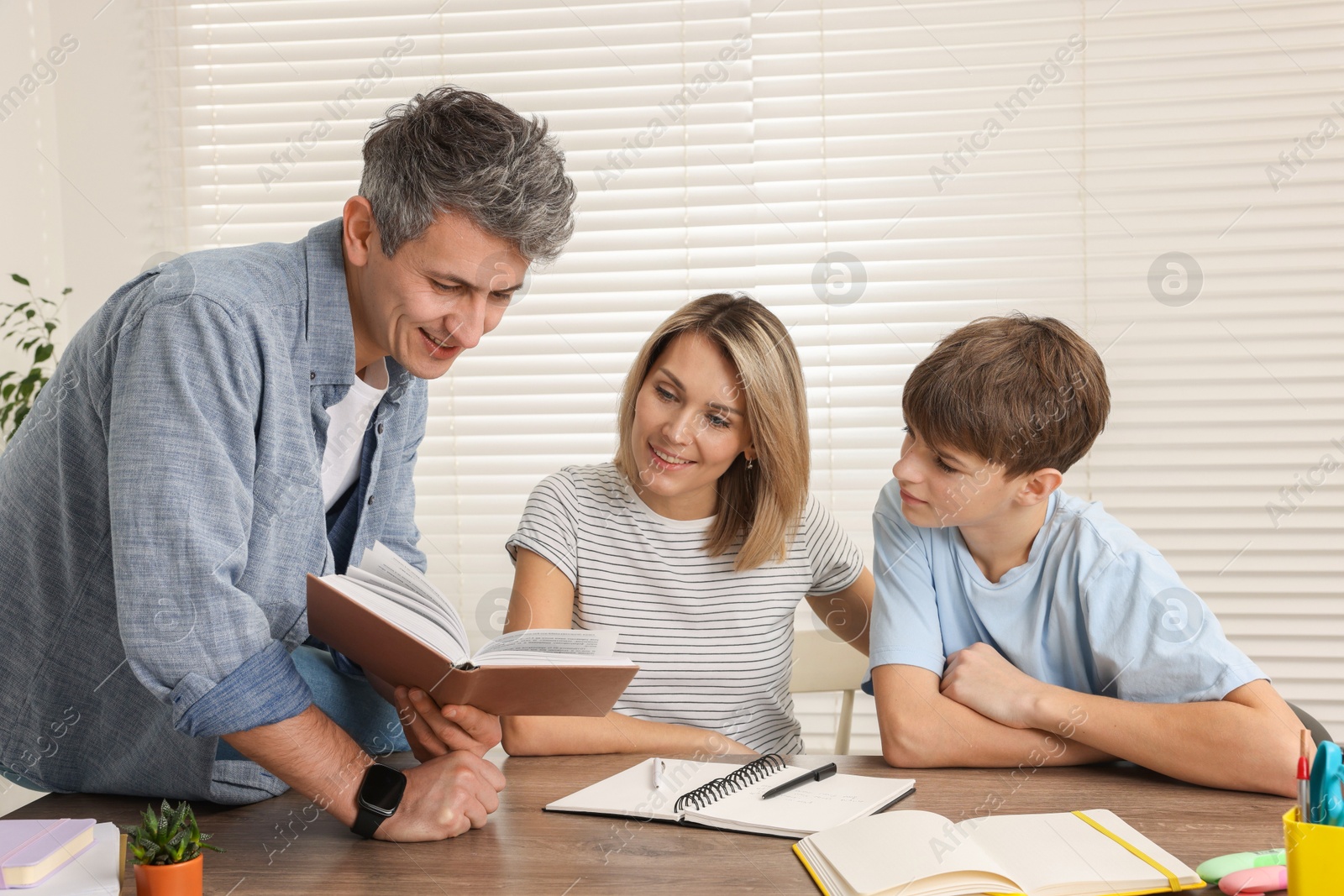 Photo of Smiling parents helping their son with homework at table indoors