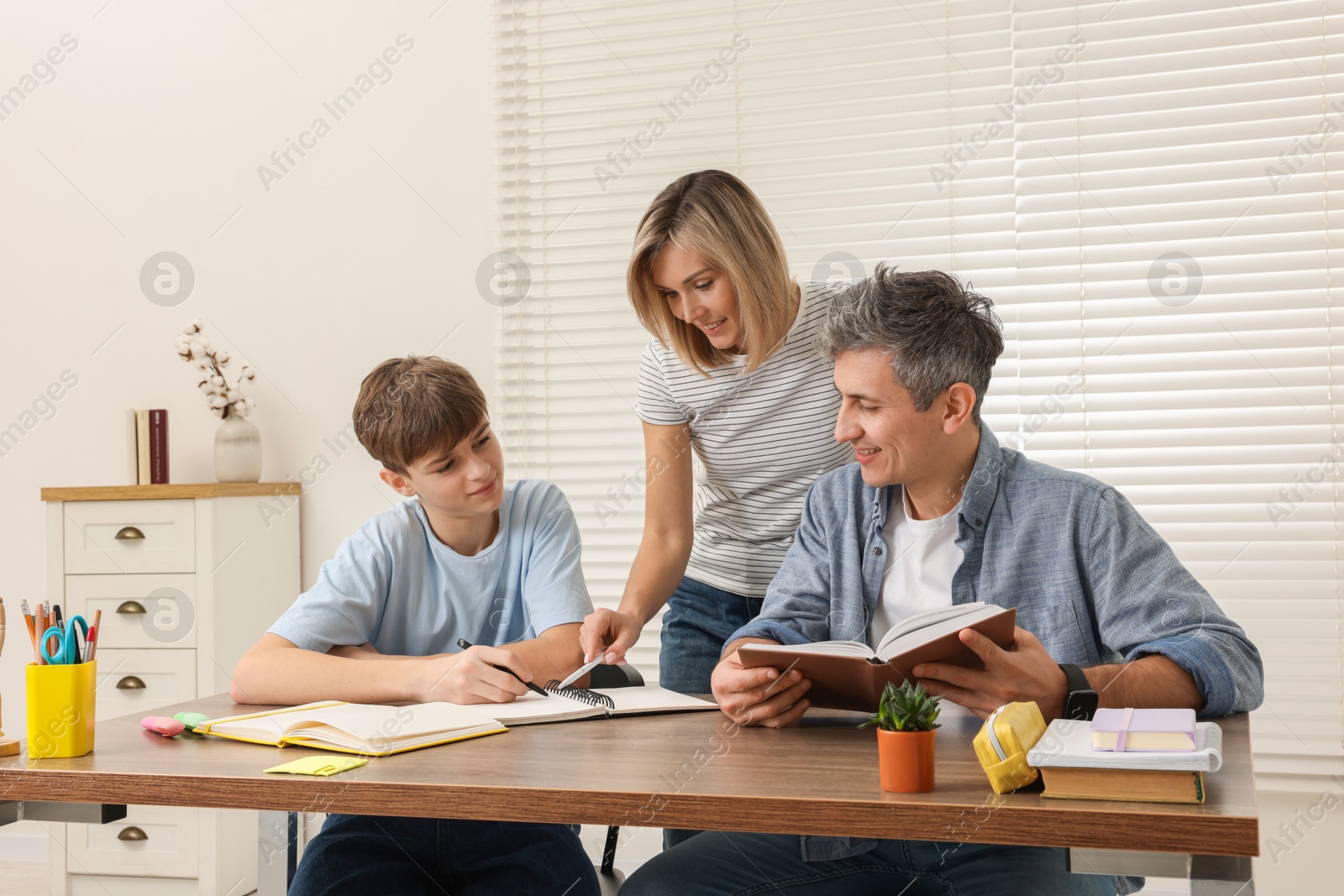 Photo of Smiling parents helping their son with homework at table indoors