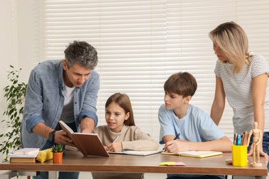 Photo of Parents and their children doing homework with laptop at table indoors