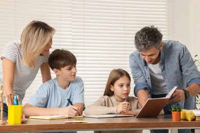 Photo of Parents and their children doing homework with laptop at table indoors