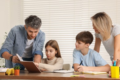 Photo of Parents and their children doing homework with laptop at table indoors