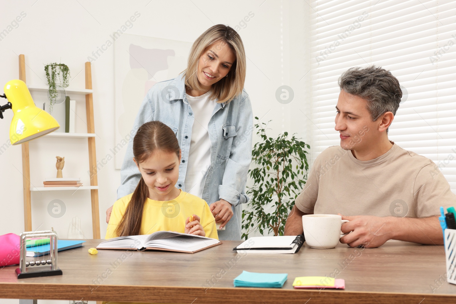 Photo of Smiling parents helping their daughter with homework at table indoors