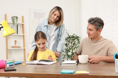 Photo of Smiling parents helping their daughter with homework at table indoors