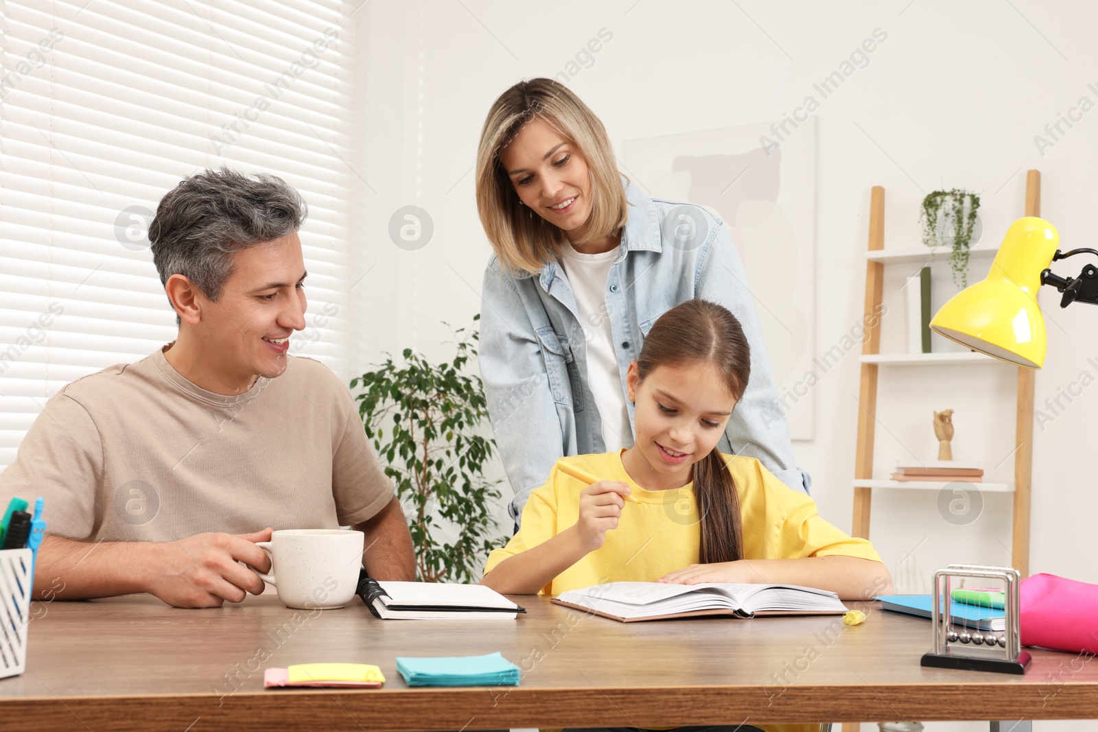 Photo of Smiling parents helping their daughter with homework at table indoors