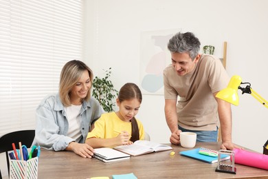 Photo of Smiling parents helping their daughter with homework at table indoors