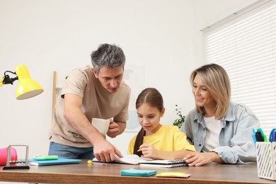 Photo of Parents helping their daughter with homework at table indoors