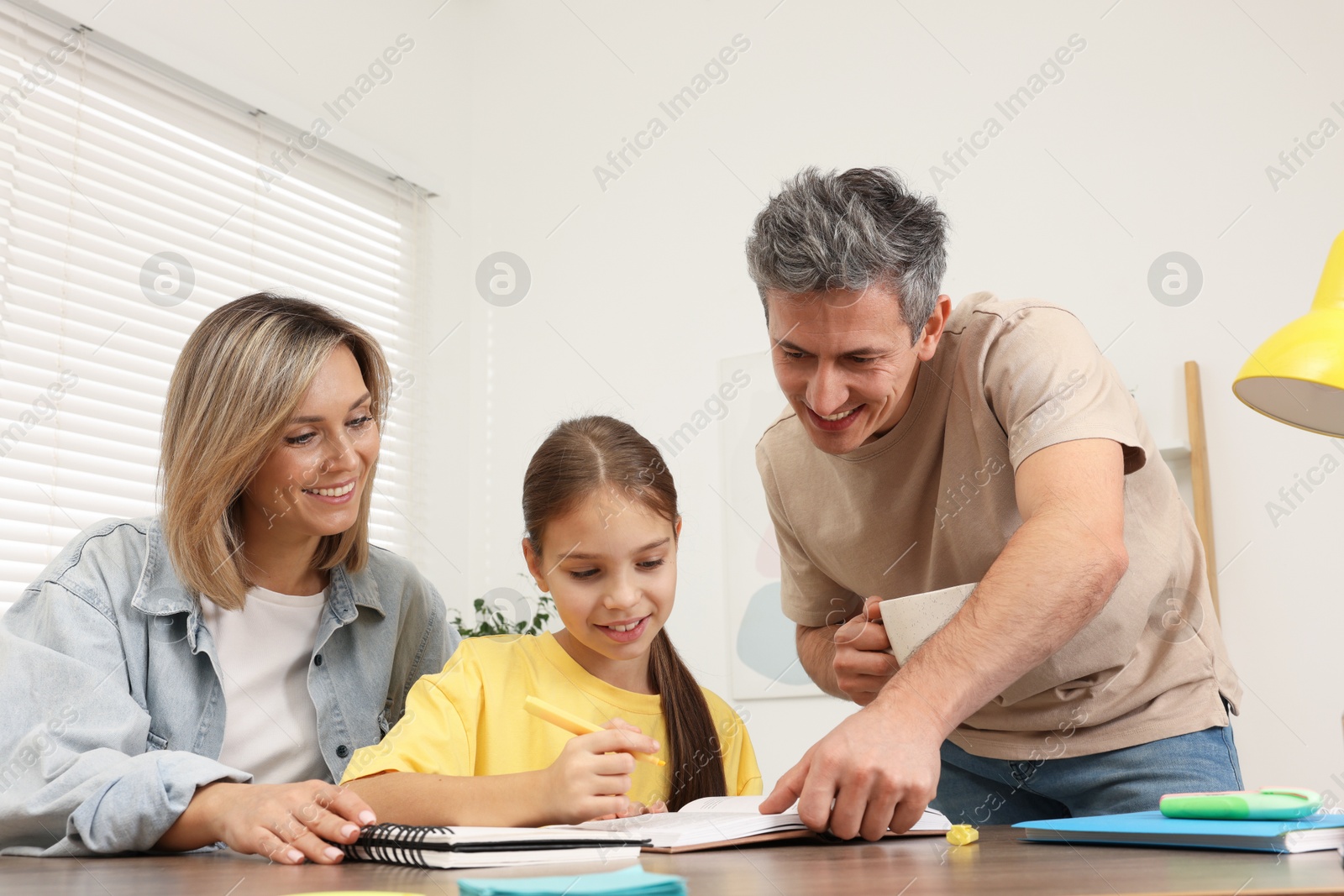 Photo of Smiling parents helping their daughter with homework at table indoors