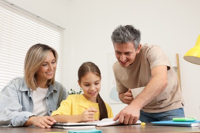 Photo of Smiling parents helping their daughter with homework at table indoors