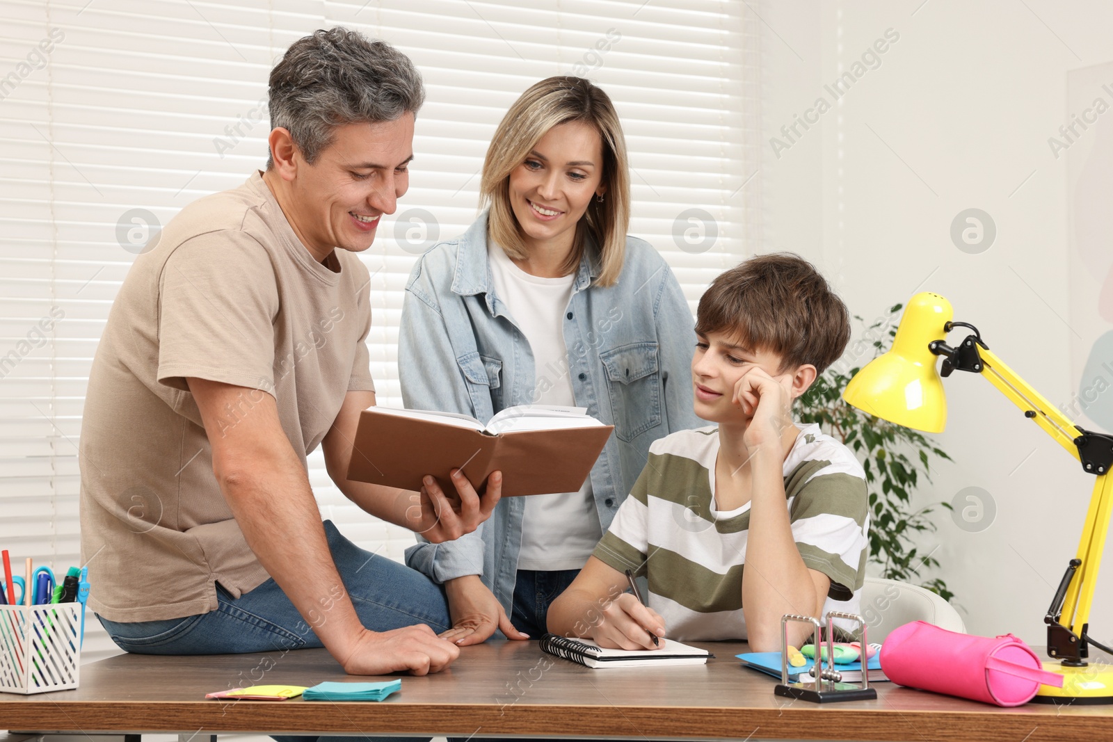 Photo of Parents helping their son with homework at table indoors