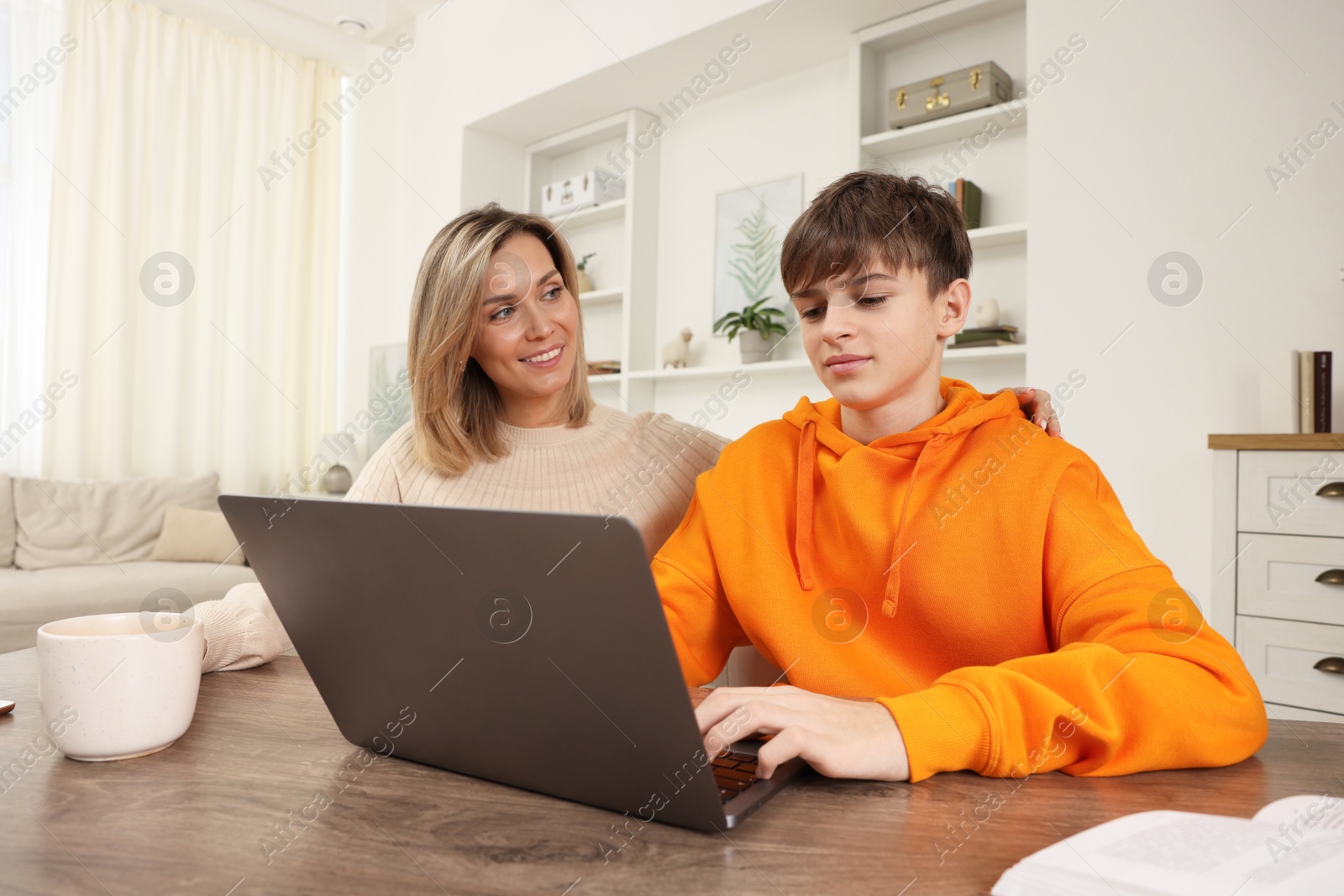 Photo of Smiling mother and her son doing homework with laptop at table indoors