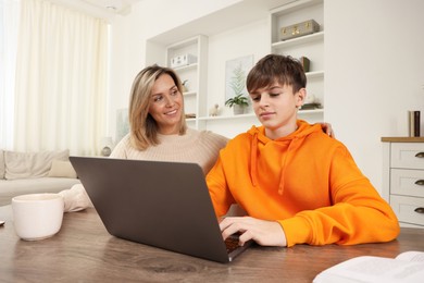 Photo of Smiling mother and her son doing homework with laptop at table indoors