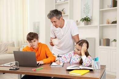 Photo of Father helping his children with homework at table indoors