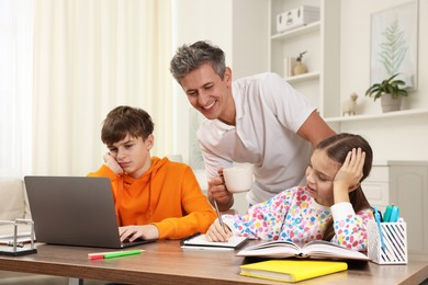 Photo of Smiling father helping his children with homework at table indoors