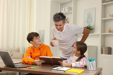 Photo of Father helping his children with homework at table indoors