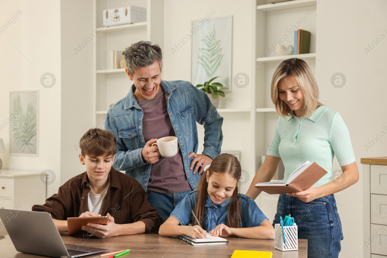 Photo of Happy parents and their children doing homework with laptop at table indoors