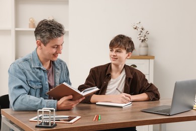 Photo of Smiling father helping his son with homework at table indoors