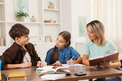 Photo of Smiling mother helping her children with homework at table indoors