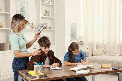 Photo of Mother helping her children with homework at table indoors. Space for text