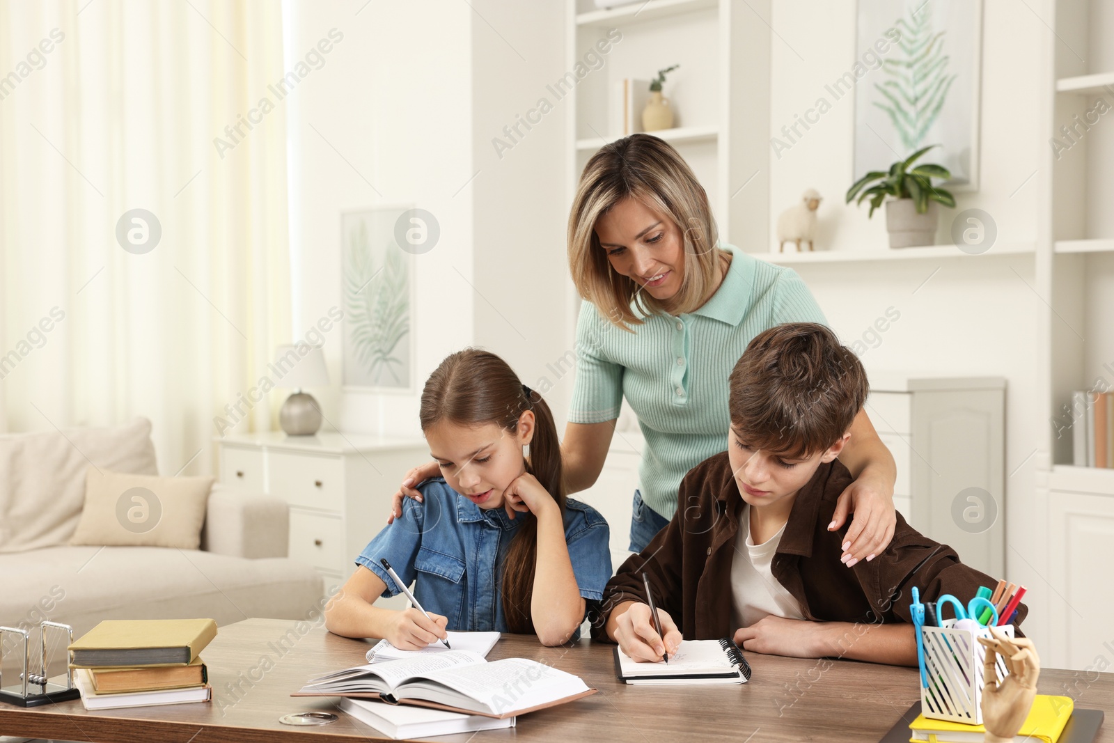 Photo of Smiling mother helping her children with homework at table indoors. Space for text