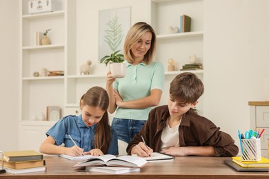 Photo of Smiling mother helping her children with homework at table indoors