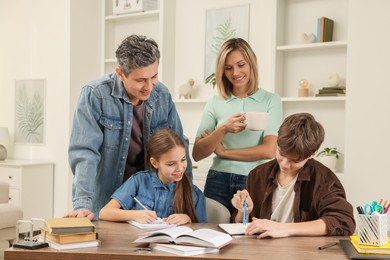 Photo of Smiling parents helping their children with homework at table indoors