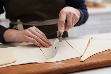 Photo of Woman cutting dough at light table indoors, closeup. Making croissants