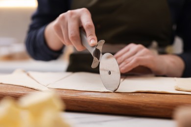 Photo of Woman cutting dough at light table indoors, closeup. Making croissants