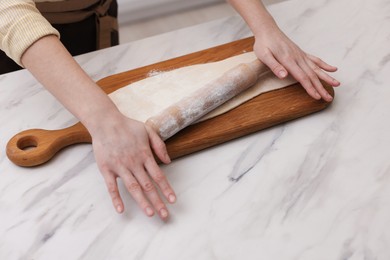 Photo of Woman rolling dough at light marble table, closeup. Making croissants