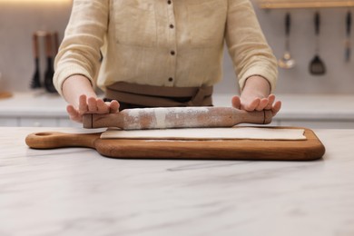 Photo of Woman rolling dough at light marble table indoors, closeup. Making croissants