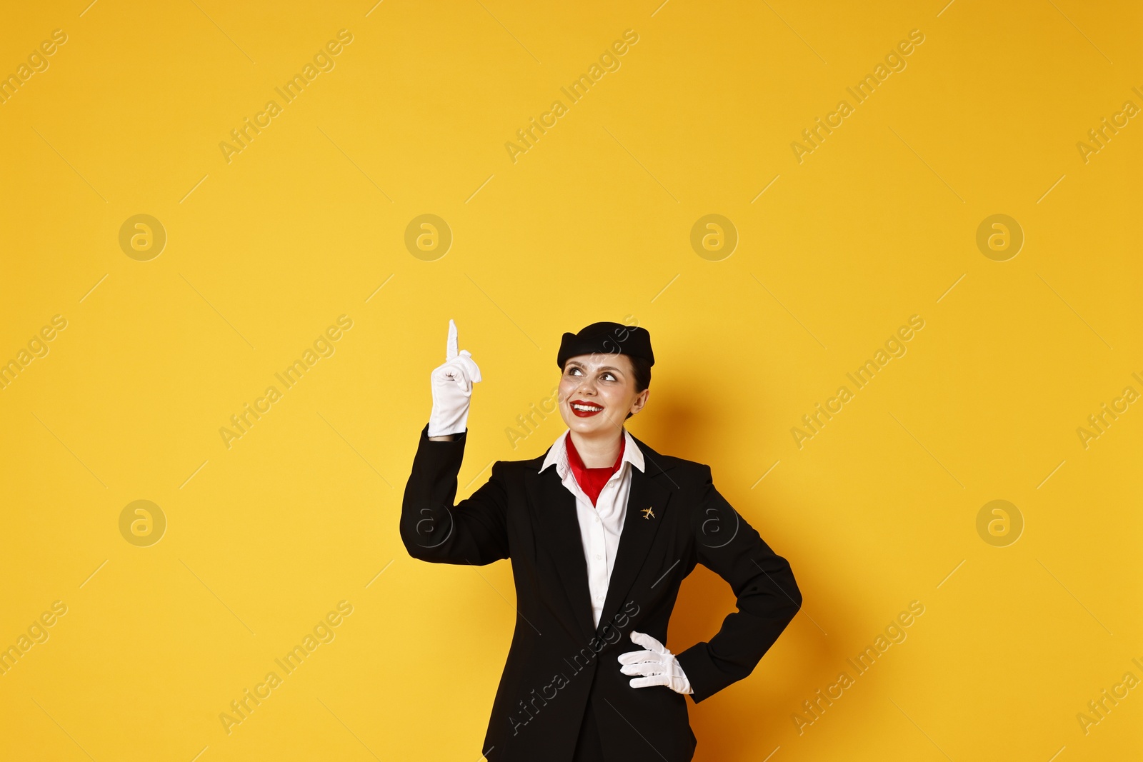 Photo of Happy flight attendant pointing upwards on orange background. Space for text