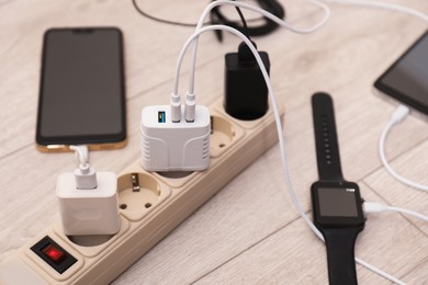 Photo of USB adapters with cables plugged into power strip charging devices on wooden floor, closeup