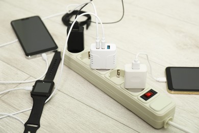 Photo of USB adapters with cables plugged into power strip charging devices on wooden floor, closeup