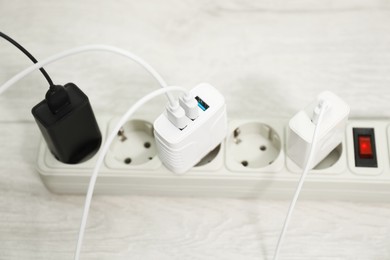 Photo of USB adapters with charge cables plugged into power strip on wooden floor, closeup