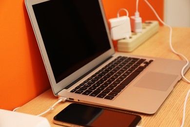 Photo of USB adapters with cables charging laptop and smartphone on wooden table near orange wall