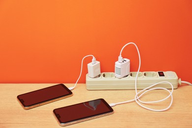 Photo of USB adapters with cables plugged into power strip charging smartphones on wooden table near orange wall