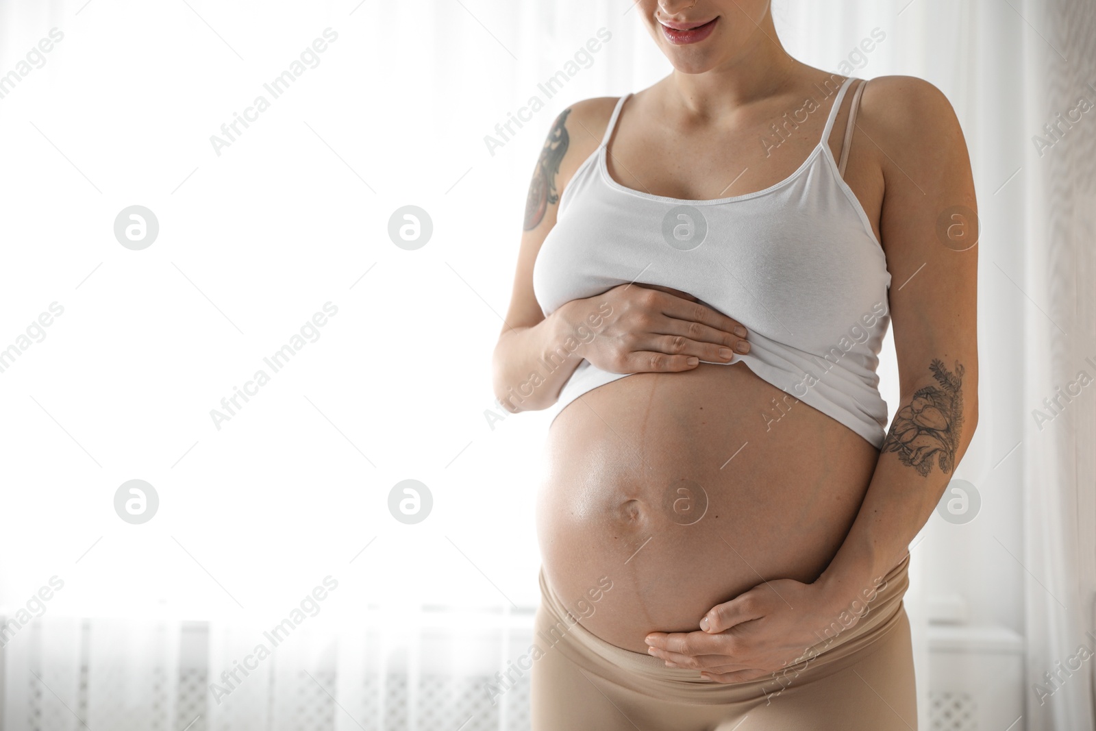 Photo of Pregnant woman near window at home, closeup. Space for text