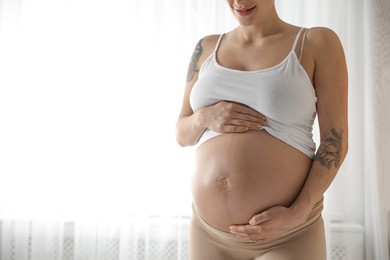 Photo of Pregnant woman near window at home, closeup. Space for text