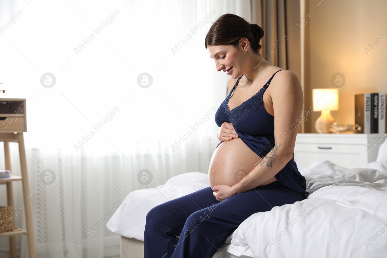 Photo of Beautiful pregnant woman on bed at home. Space for text