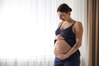 Photo of Beautiful pregnant woman near window at home. Space for text